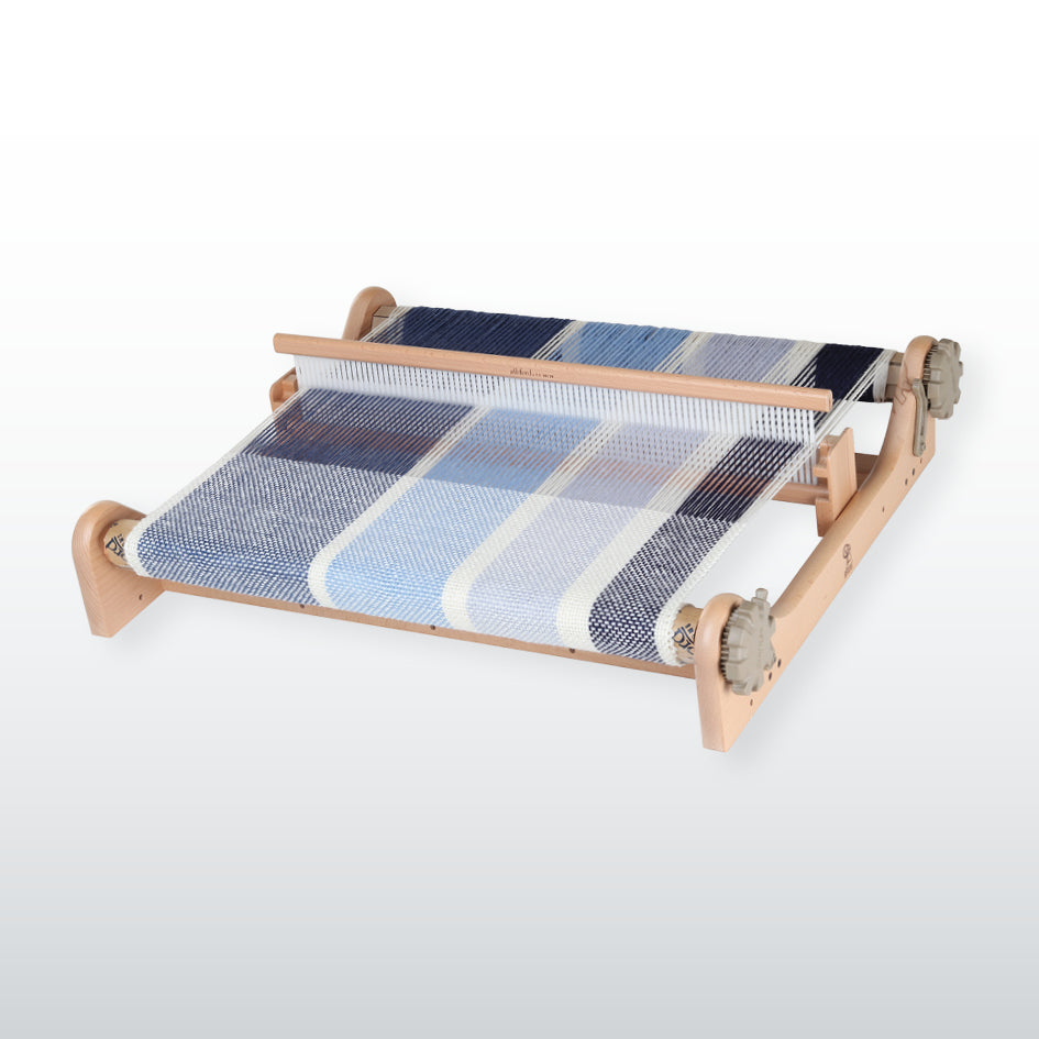Ashford Rigid Heddle Loom made of light colored wood, with a woven fabric on the loom and yarn threaded through the heddle and reed