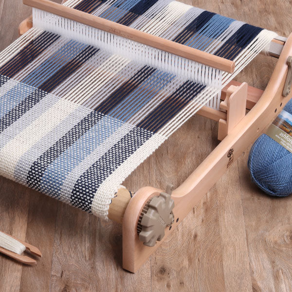 Close up of an Ashford Rigid Heddle Loom showing the heddle with threads passing through the slots and holes, and the woven fabric emerging below.