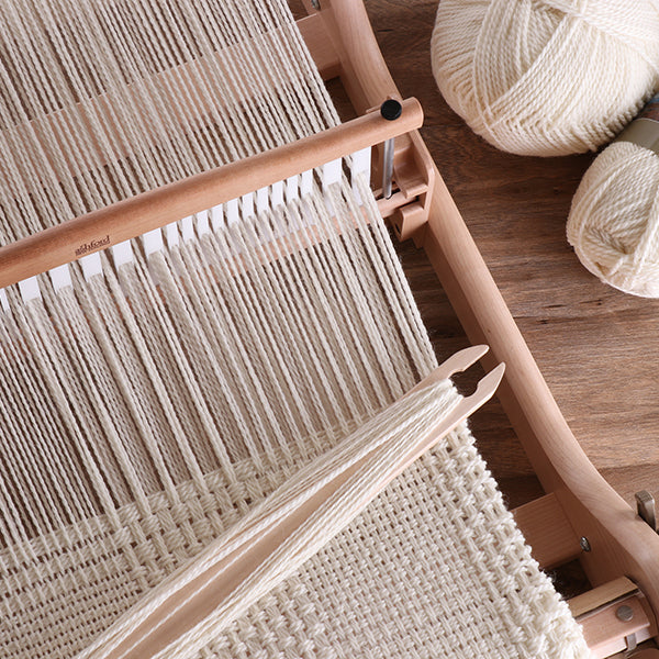 Close up of weaving yarn threaded through the heddle of a rigid heddle loom, highlighting the texture and alignment of the warp threads.